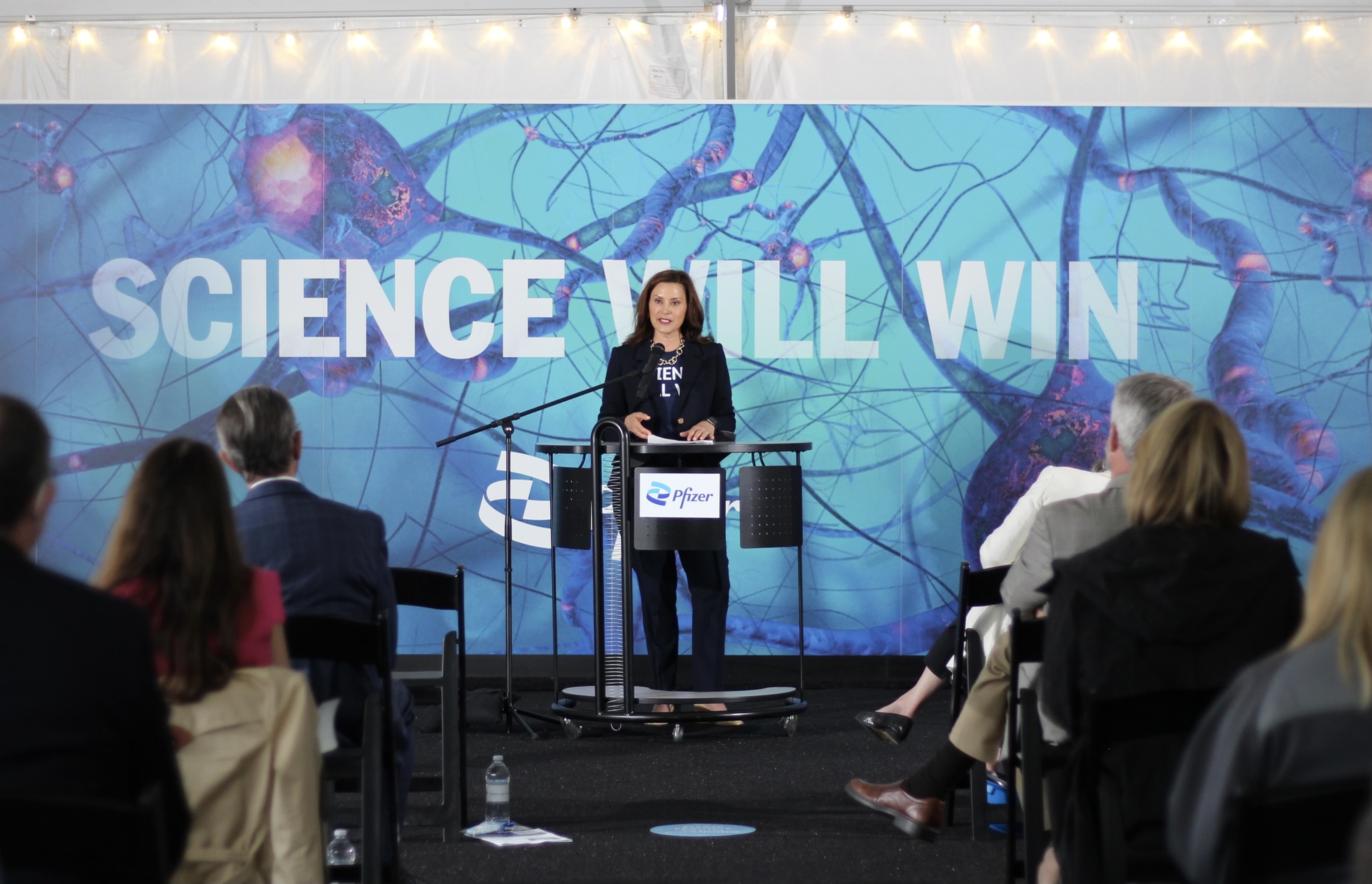 Gov. Whitmer speaks at podium during Pfizer event. Behind her, a banner reads 